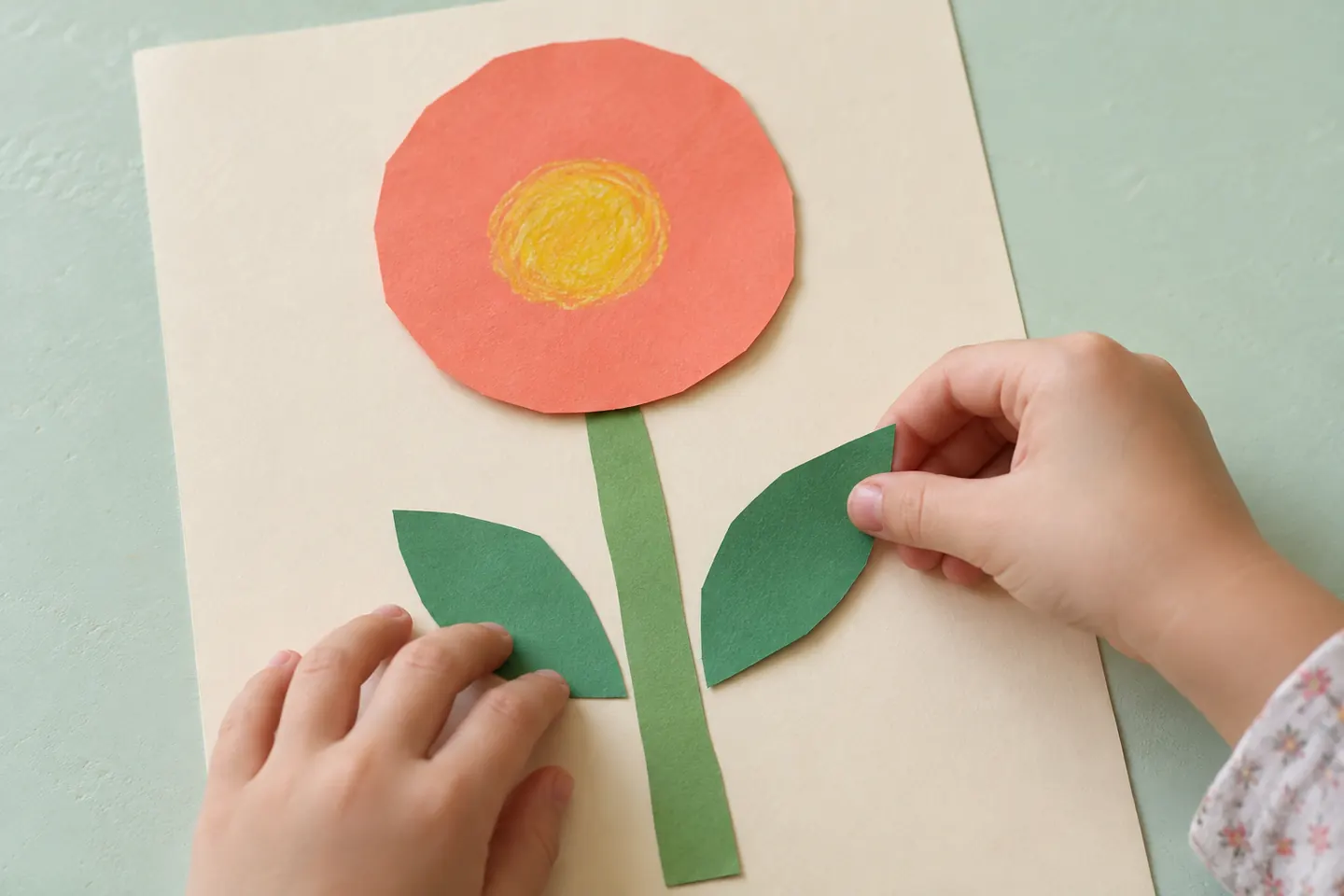 A coral paper flower arranged with a broad stem and two leaves.