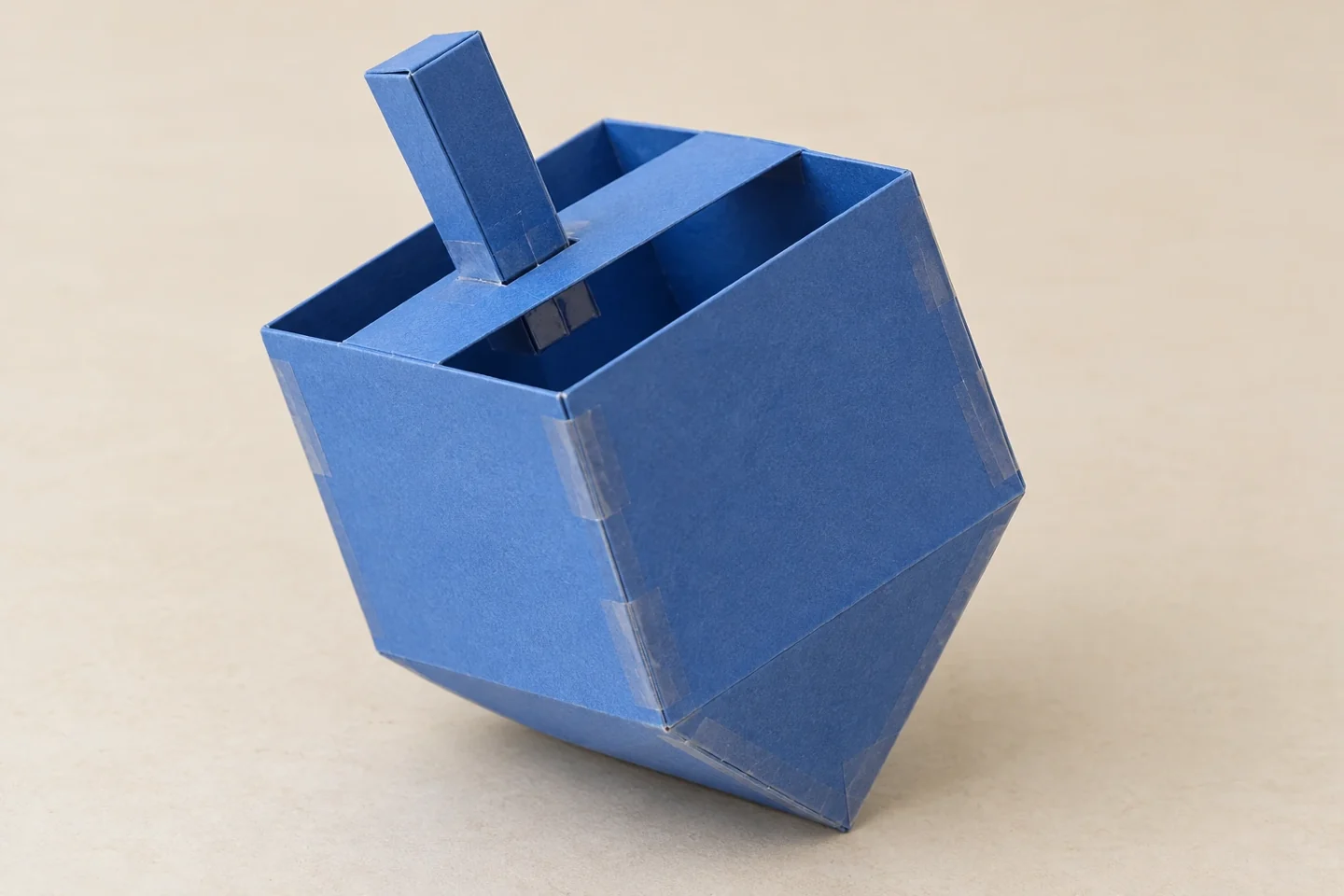 One upright-on-its-side hollow cardstock dreidel display model, square body pointed lower pyramid and short folded-paper handle; no invented Hebrew marks