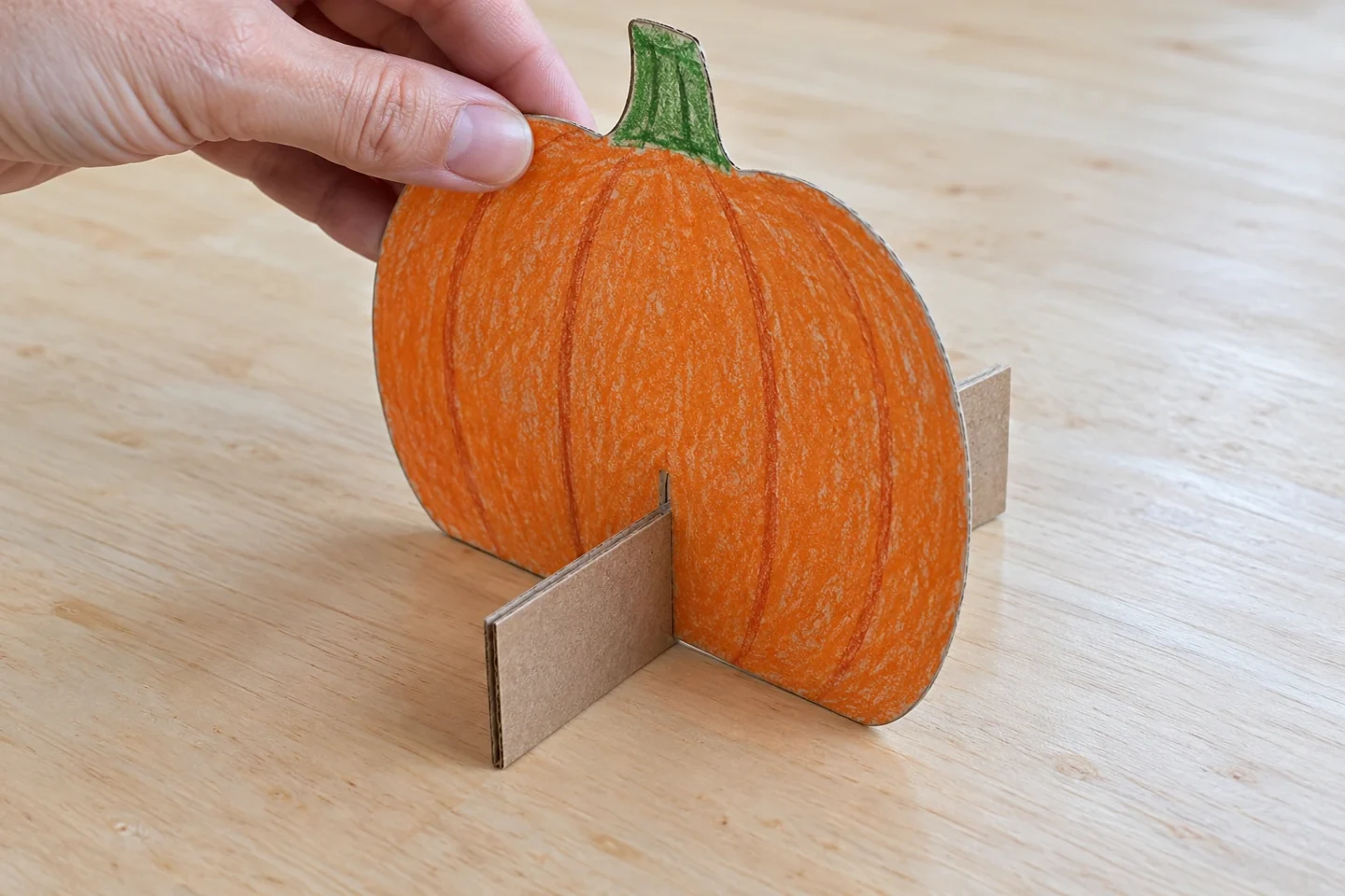 One orange pumpkin slots into a rectangular cardboard base at a right angle, with both lower edges on the table.