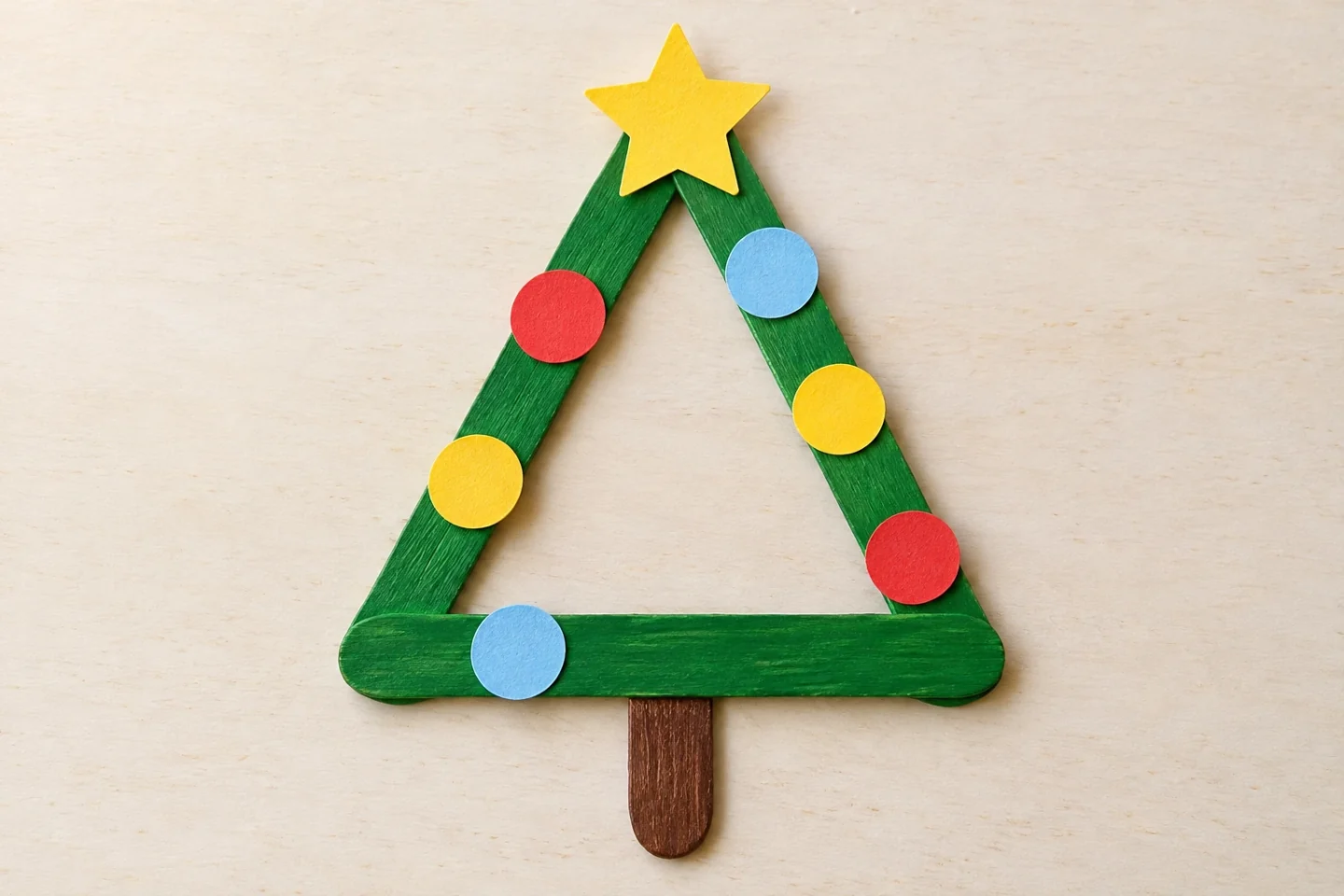 One finished green open triangle tree with brown short trunk, six small paper circles and one yellow star, lying flat and fully dry