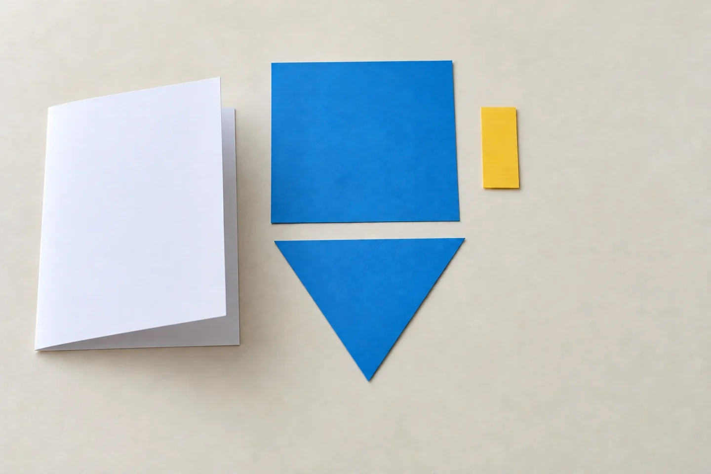 Folded blank portrait card beside one blue square body, blue downward triangle point, yellow short rectangular handle and loose white border pieces