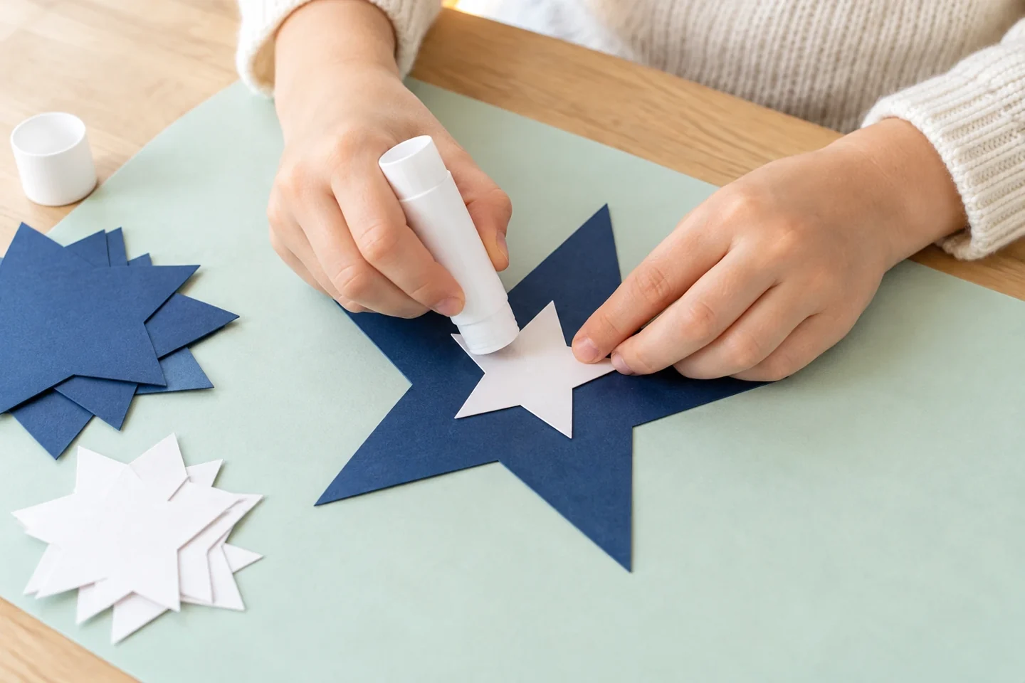 Hands gluing a small white paper star onto a navy star