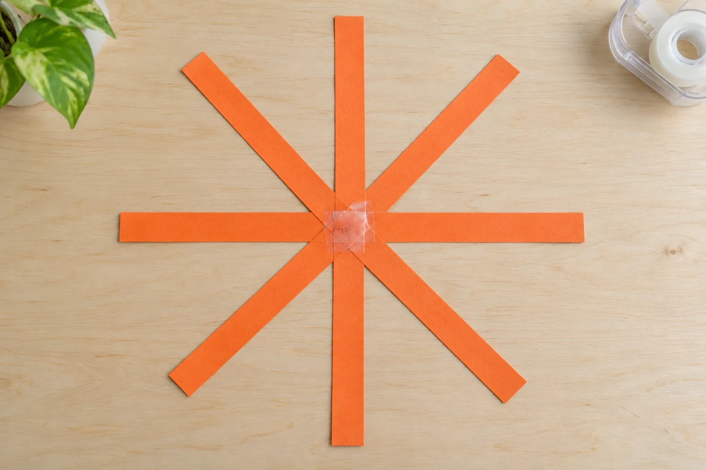 Eight orange strips arranged as flat spokes and taped together at one central join.