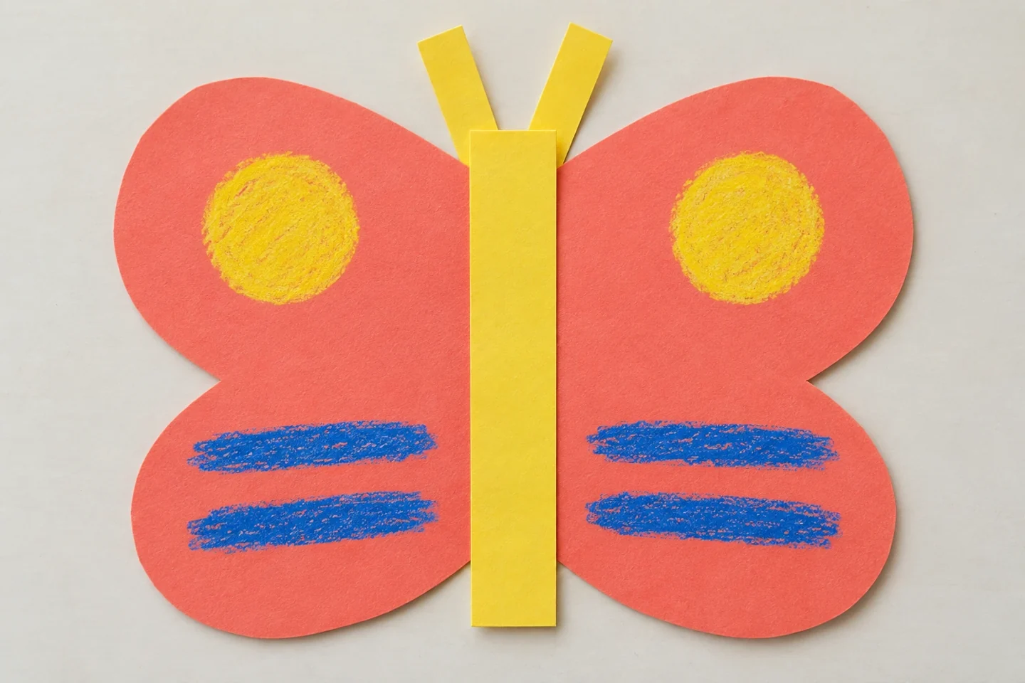 connected coral wings with mirrored yellow circles and blue stripes, yellow paper body on crease and two short wide paper antennae, ordinary child craft finish